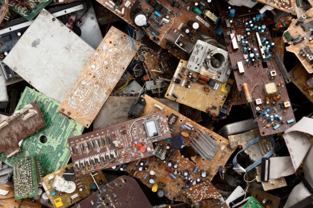 A chaotic pile of discarded electronic circuit boards lies in an Atlanta, GA facility, featuring various components and wires. The boards are densely packed, with diverse colors and intricate soldered connections visible throughout—an urgent reminder of the importance of electronic recycling.