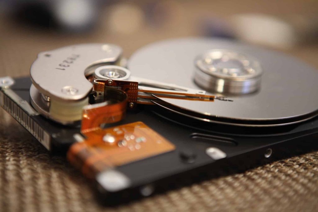 Close-up of an open hard disk drive showing the shiny silver platters and read/write head arm. The circuit board and drive casing are partially visible in the foreground, illustrating the intricate technology behind devices often destined for electronic waste in Atlanta, GA.