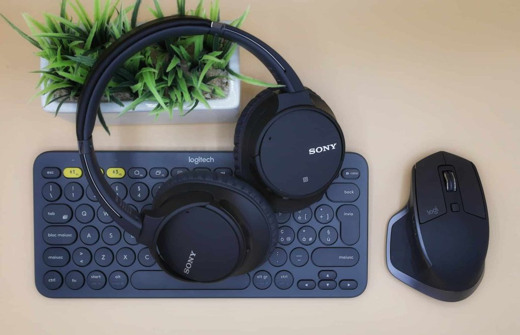 A Sony wireless headphone rests on a Logitech keyboard, with a Logitech MX Master mouse beside them, all poised for electronic recycling in Atlanta, GA. A small green plant adds life to the scene on the wooden table.