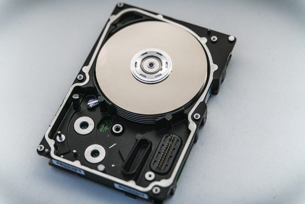 Close-up of an exposed internal hard disk drive showing the shiny, round platters and read/write head. The device, a common candidate for electronic waste recycling in Atlanta GA, rests on a plain surface, highlighting its mechanical components ready for disposal.