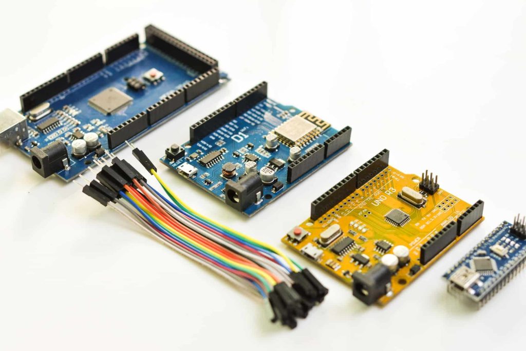 A collection of colorful circuit boards and microcontrollers with attached wires is laid out on a white surface. The boards, perfect for electronic recycling in Atlanta GA, vary in size and color, featuring diverse electronic components and connectors.