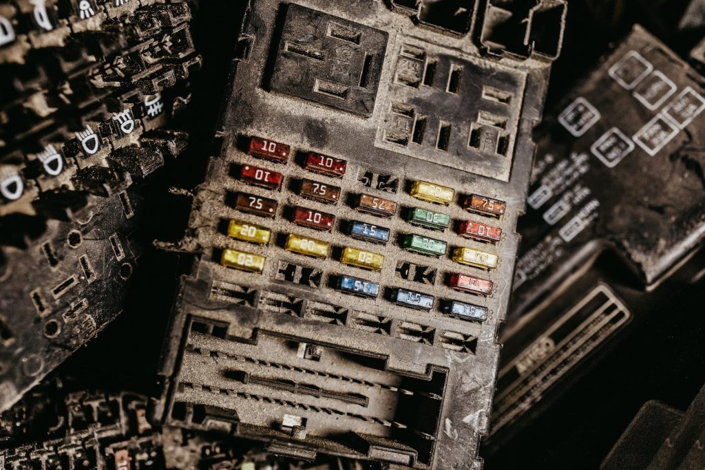 Close-up of a dusty, old fuse box with colorful fuses in red, yellow, blue, and green, each labeled with different amperages. The wear suggests long-term use or obsolescence, typical in industrial contexts. Perfect for electronic recycling enthusiasts in Atlanta GA seeking vintage components.