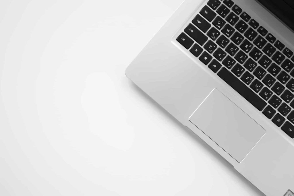 A partial view of an open laptop with a silver body and black keyboard, placed on a white surface, evokes modernity and minimalism. The top right corner of the keyboard and the trackpad are captured, highlighting its sleek design—ideal for responsibly recycling at an Electronic Waste center in Atlanta GA.