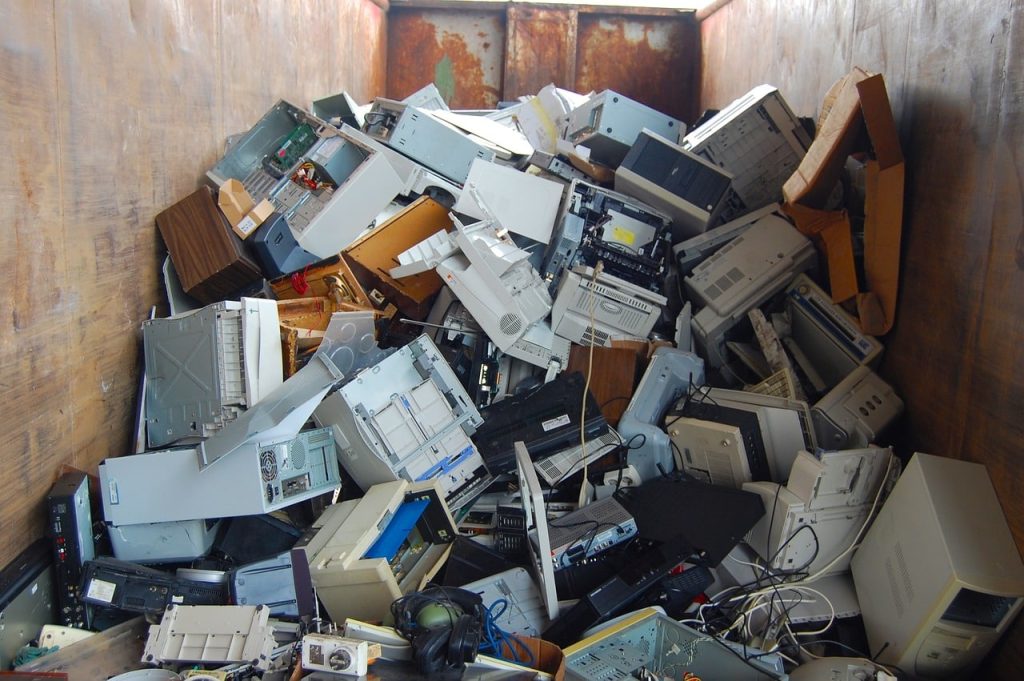 A large pile of electronic waste, including old computer towers, printers, and cables collected for Electronic Waste Atlanta GA recycling initiatives, fills a rusty metal container.