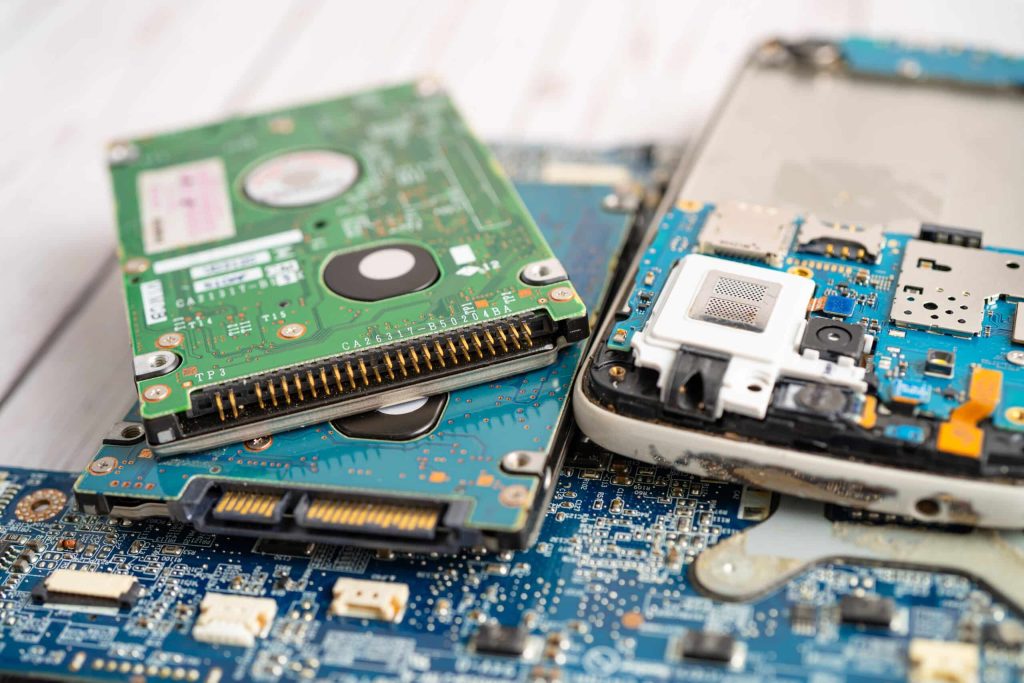 Close-up of electronic components, including a hard drive, circuit boards, and various connectors, placed on a light wooden surface. The image showcases the intricate details of hardware destined for electronic recycling in Atlanta GA.