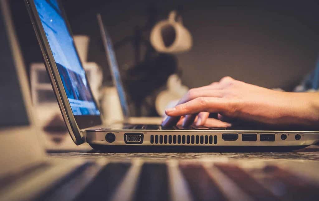 In a dimly lit room, a person types on a laptop keyboard, surrounded by another laptop and hints of an office backdrop. The scene evokes the bustling creativity of Electronics in Atlanta GA.