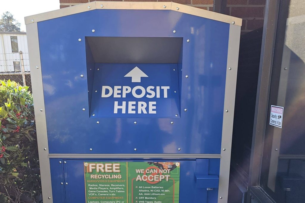 A blue recycling deposit bin with a "Deposit Here" sign is located outside a building in Atlanta, GA. Below, you'll find detailed lists of acceptable items for electronic recycling and non-acceptable ones, along with a QR code and contact information for electronics disposal inquiries.