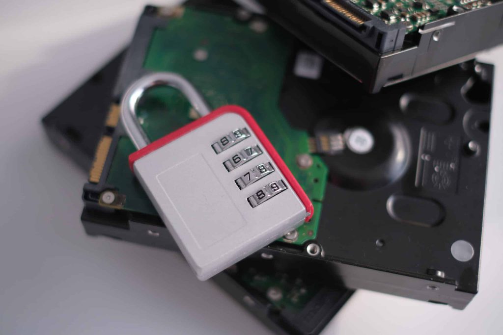 A combination padlock rests on a stack of computer hard drives, hinting at secure measures for electronics. The lock reads "1-5-8" while the blurred backdrop emphasizes its prominence. Consider Electronic Recycling Atlanta GA for proper disposal of such devices.