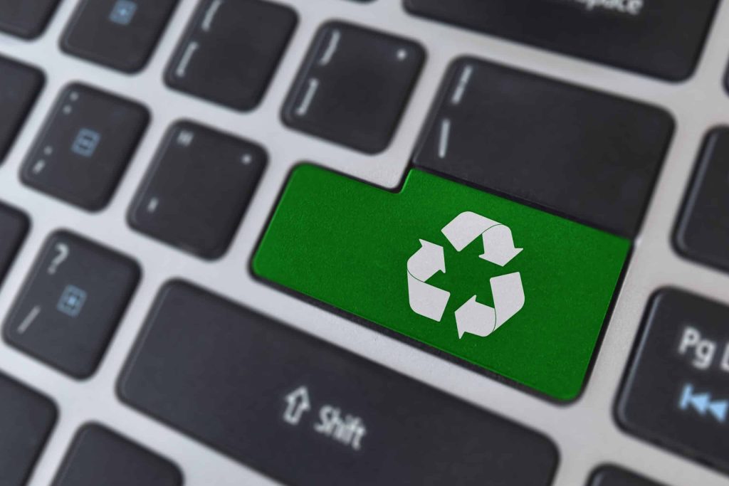 A close-up of a keyboard with a green Enter key displaying a white recycling symbol, highlighting the importance of electronic waste recycling. Situated in Atlanta, GA, this encourages users to consider using local drop-off boxes for responsible disposal. Surrounding keys are black, emphasizing the distinct green key.