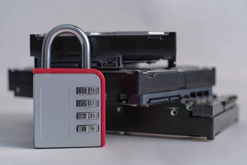 A combination lock stands in front of a stack of three black hard drives, symbolizing data security. Nearby, a drop-off box in Atlanta, GA awaits electronic waste and recycling, reinforcing the theme of protection for both data and the environment.