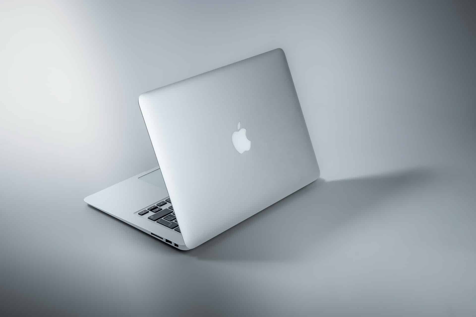 A silver laptop with a glowing apple logo rests slightly open on a smooth, reflective surface, casting a soft shadow against the minimalist, monochromatic background. Perfect for those interested in electronics in Atlanta, GA.