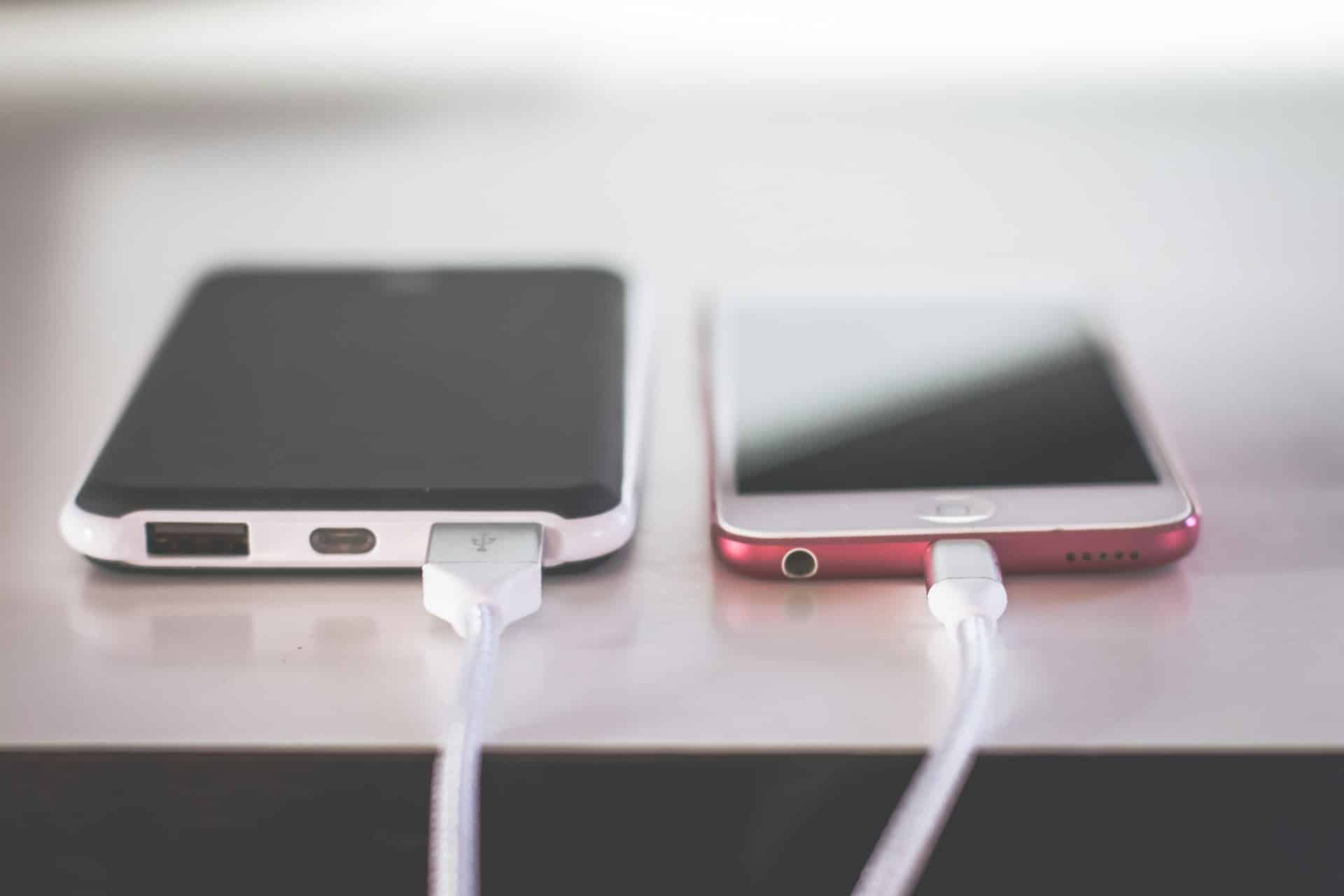 Two smartphones on a table charging with white cables. The phone on the left has a black and white case, while the one on the right appears to be pink. If you're upgrading, consider using an electronic waste drop-off box in Atlanta, GA for responsible disposal.