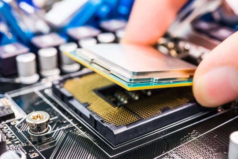 Close-up of a person's hand installing a computer processor into a motherboard socket. The image captures the delicate process of aligning the processor with socket pins, highlighting the importance of electronics recycling in reducing e-waste disposal against a backdrop of electronic components.