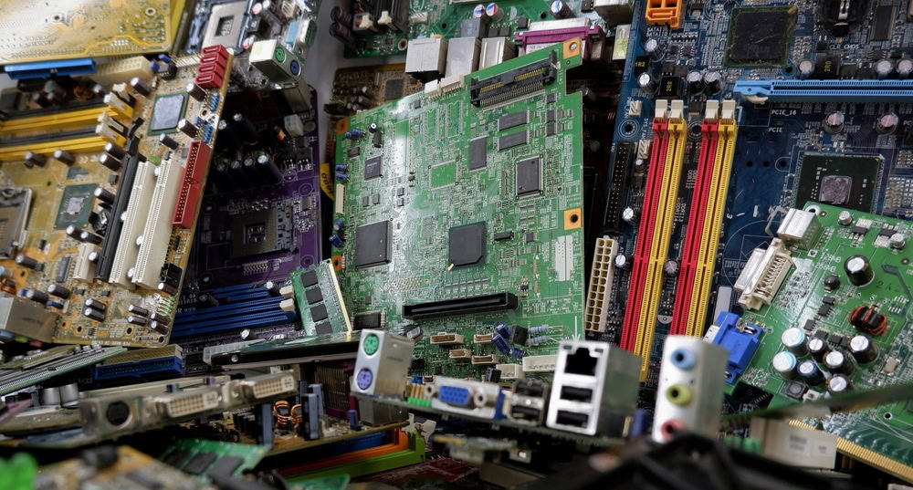 A pile of various colorful circuit boards, including motherboards and other electronic components, with visible ports and connectors. In this chaotic arrangement of greens, blues, and yellows lies a reminder to recycle laptops responsibly to address E-waste disposal effectively.